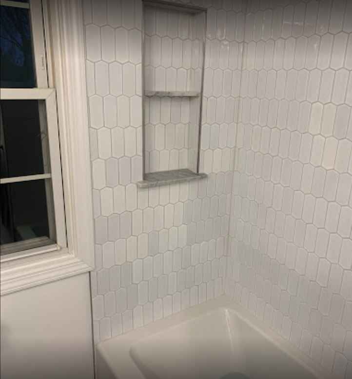 White tiled bathroom corner with a bathtub and window shelf niche