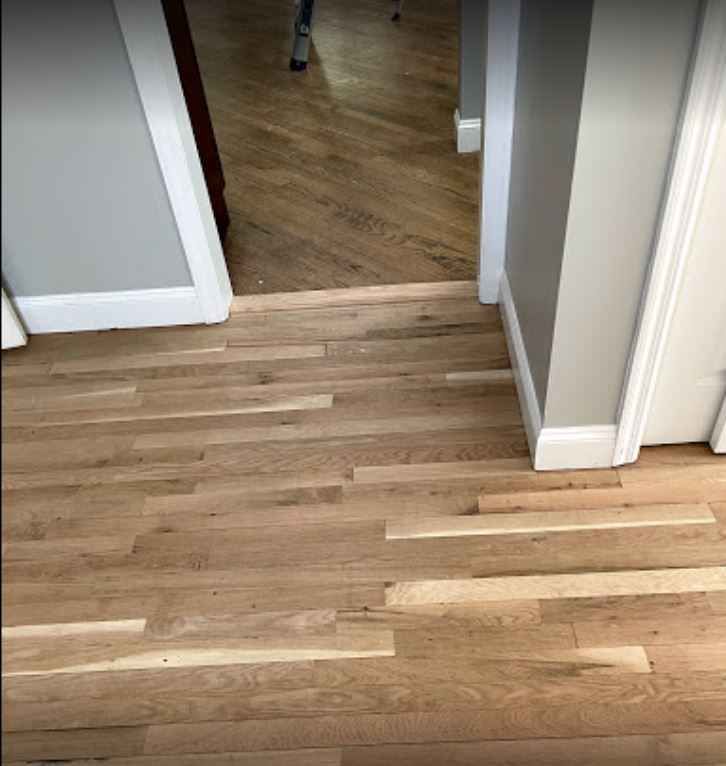 Hardwood hallway floor with a small raised threshold between rooms and white baseboards