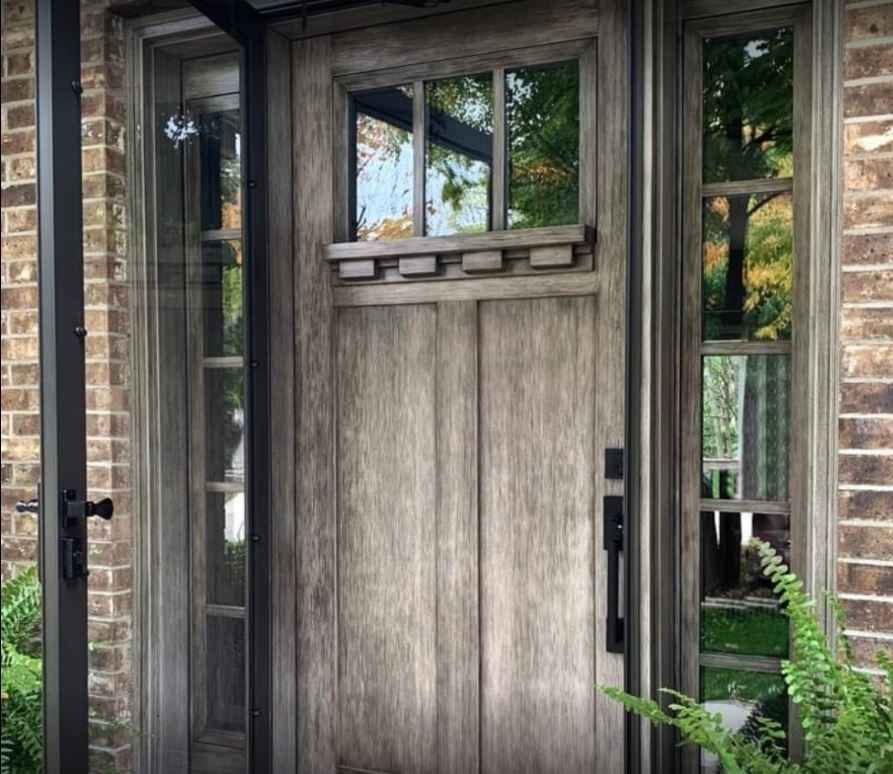 Wooden front door with sidelights and a small window, set in a brick entryway.