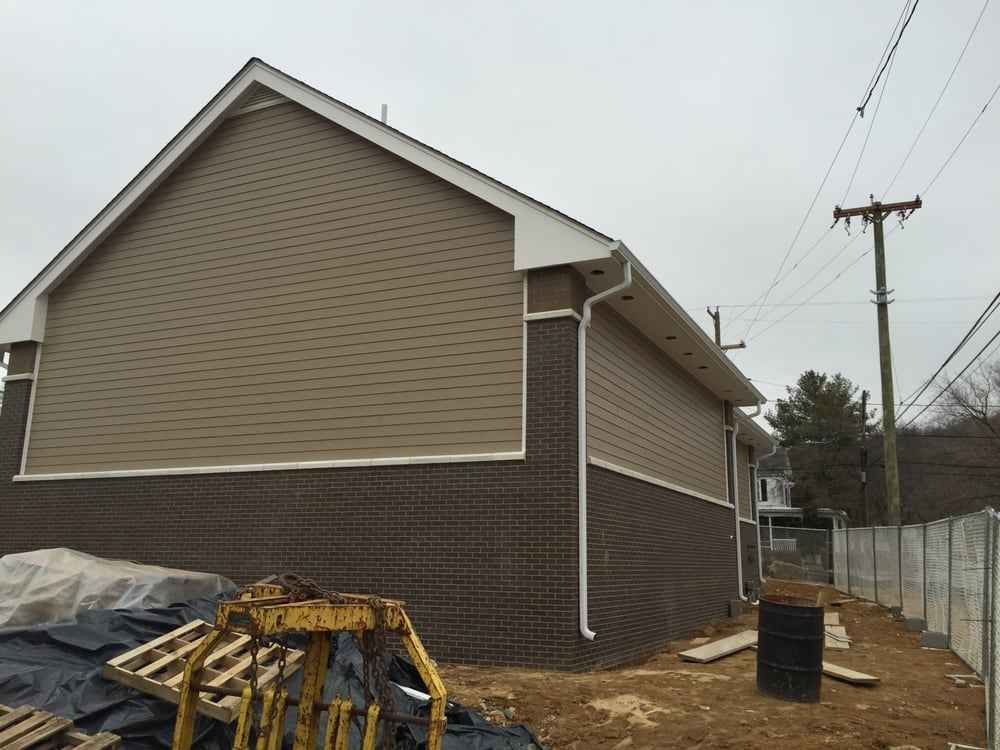 House exterior with tan siding and dark brick, construction materials in the yard, and utility poles nearby
