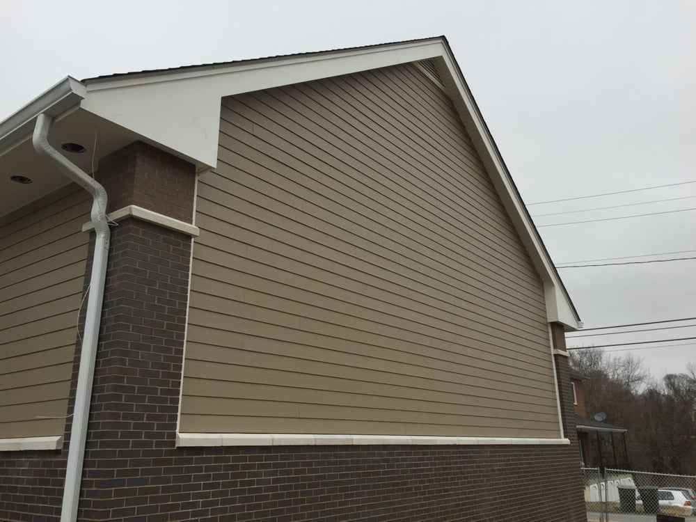 Exterior of a beige house with dark brown brick siding and white trim under an overcast sky