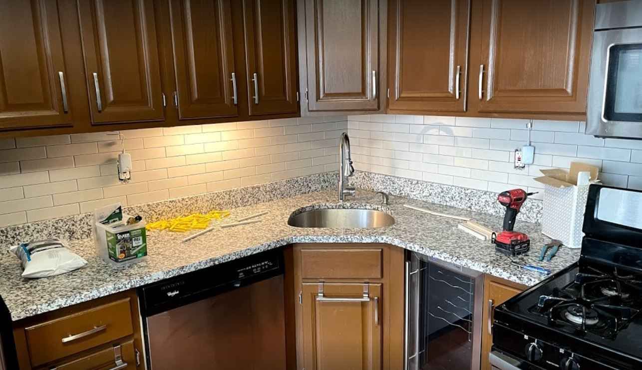 Corner kitchen with dark wood cabinets, granite countertops, and a black stove beneath a tiled backsplash.