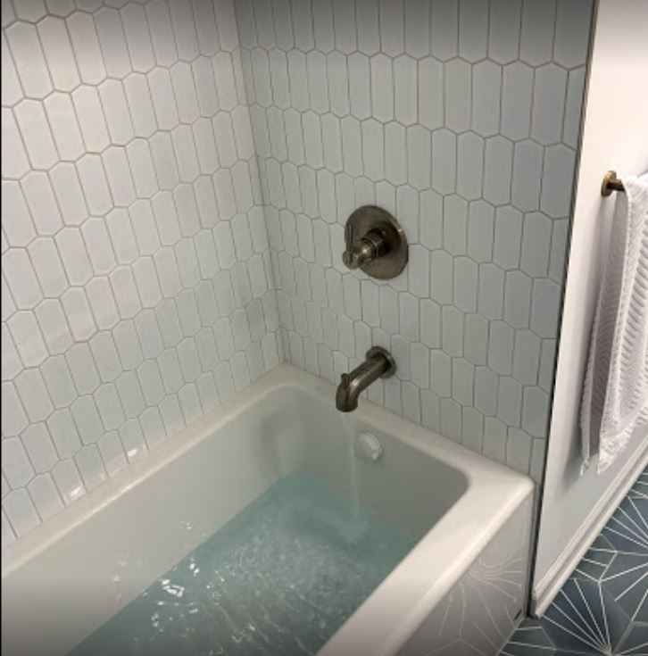 Empty white bathtub with faucet and hex tile shower wall in a bathroom