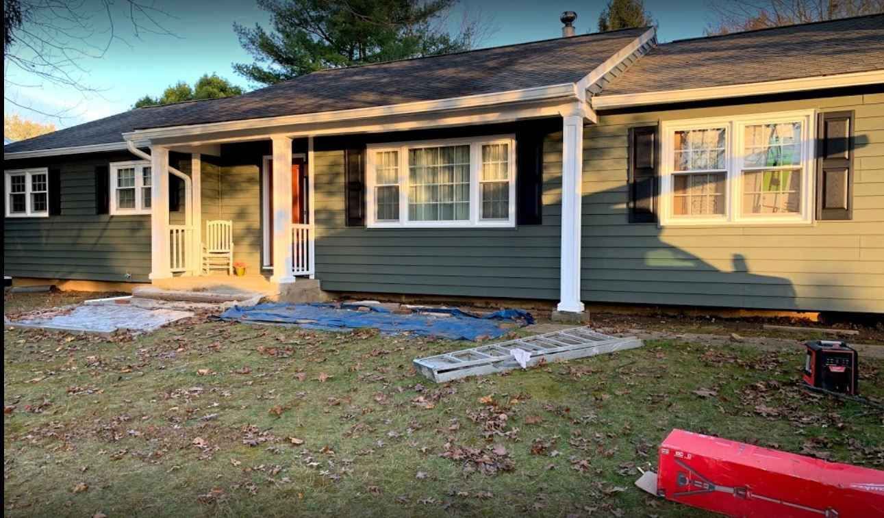 Single-story house with green siding, front porch, and sunlit yard in early evening.