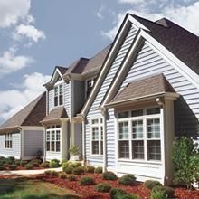 Suburban row of beige and white townhouses with brown roofs and landscaped flower beds under a cloudy sky