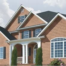 Brick suburban house with white columns, arched porch, and dark shingle roof against a cloudy sky