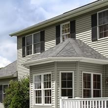 Gray house with white trim and bay window under a cloudy sky