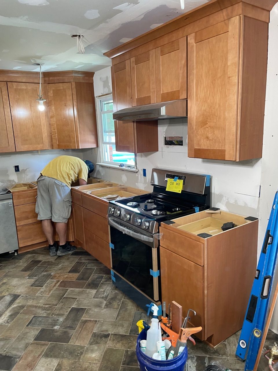 Kitchen renovation in progress, with person working at countertop beside stove and wooden cabinets.