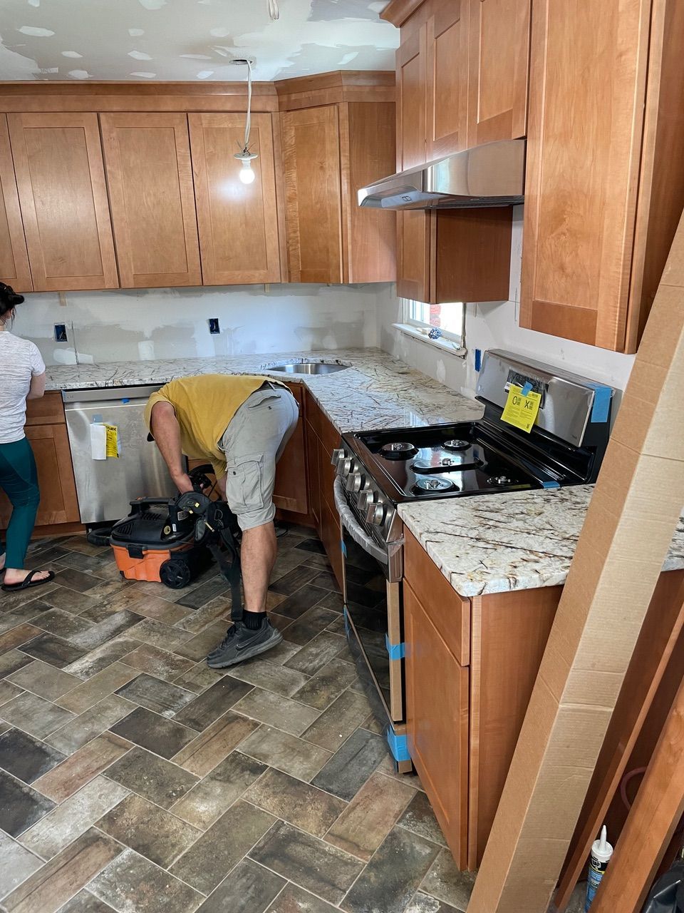Two workers installing a granite kitchen countertop in a wood-cabinet kitchen
