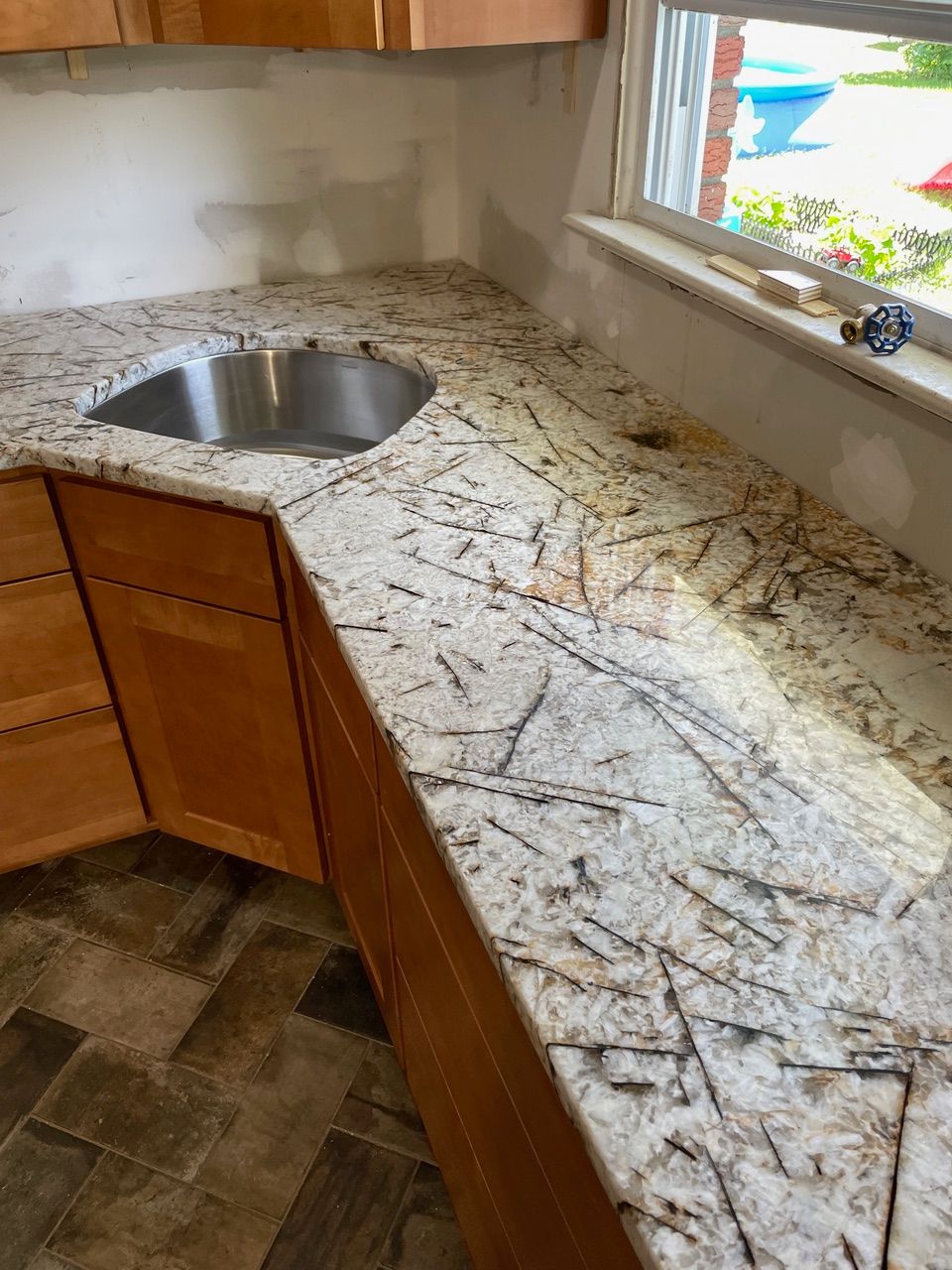 Kitchen corner with granite countertop, stainless sink, wood cabinets, and tiled floor by a window.