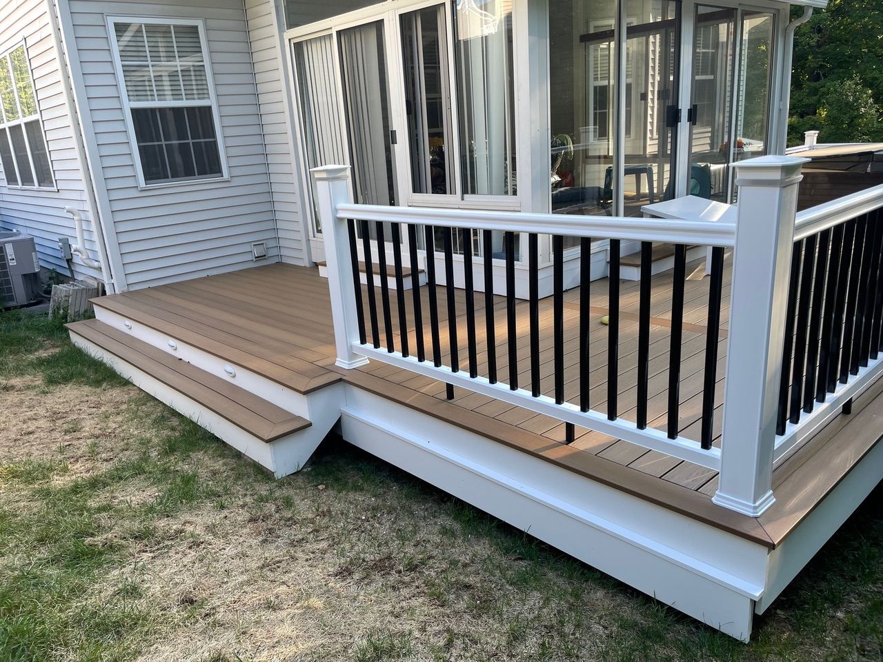 White house deck with steps, railing, and screened porch over patchy grass