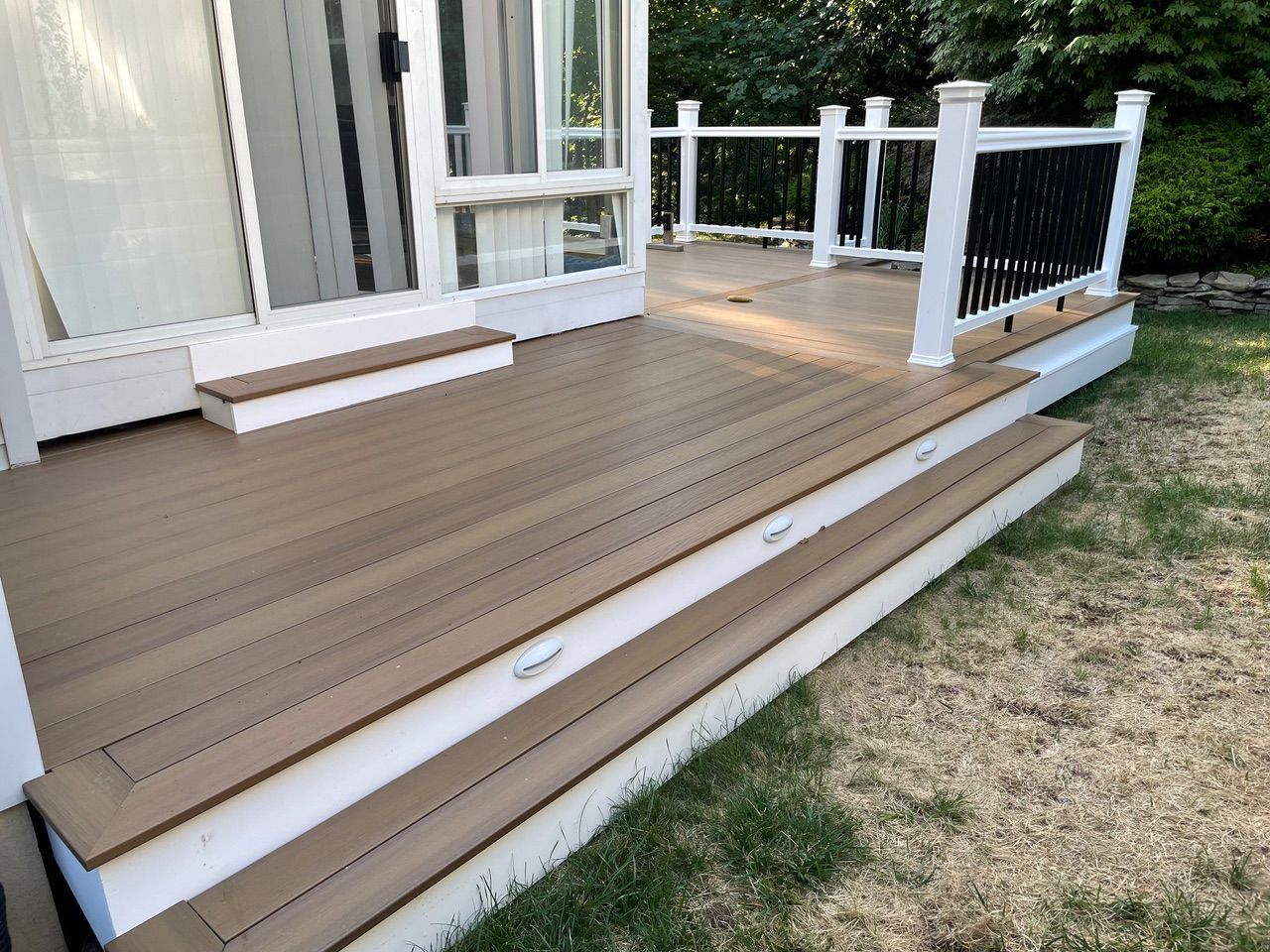 Brown wooden deck with white railings and steps beside a grassy yard