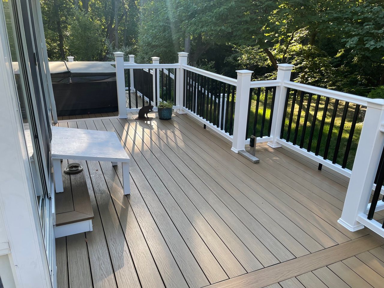 White deck with railing, patio table and chairs, and potted plants in bright sunlight.