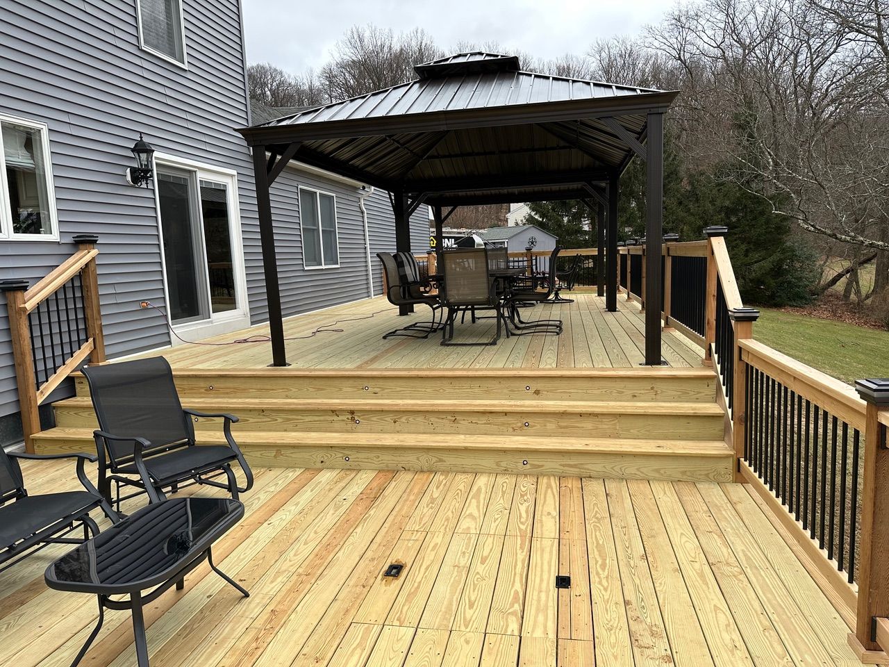 Wooden deck with railing, steps, and covered seating area beside a gray house.