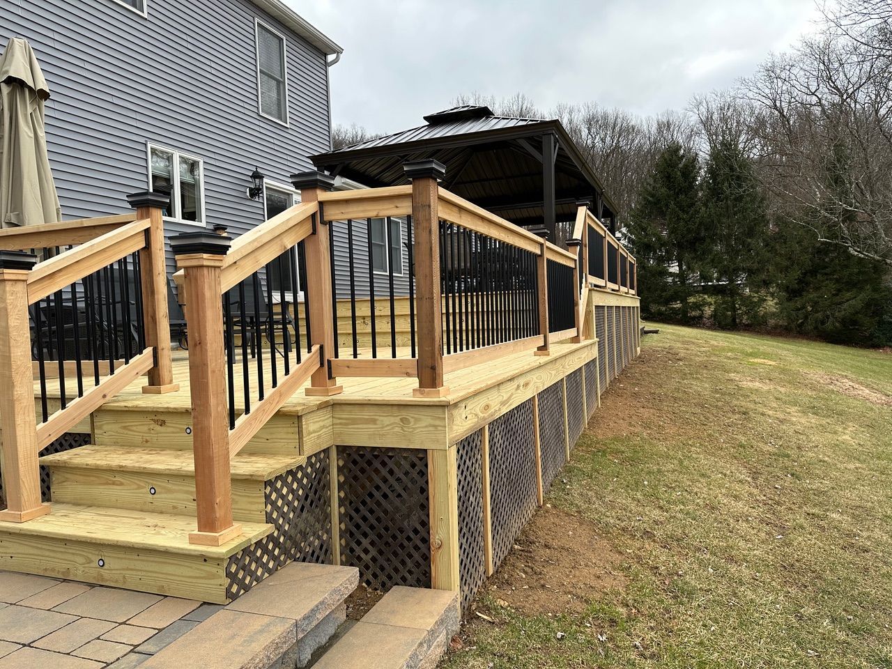 Wooden accessibility ramp and stairs beside a house, with black railings and a covered landing.