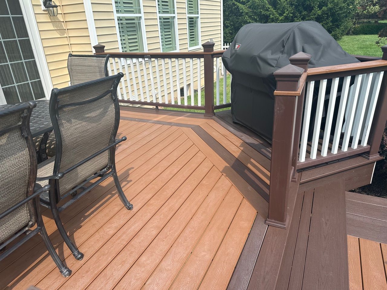 Wooden deck with black mesh chairs and a covered grill beside a brown railing and house siding