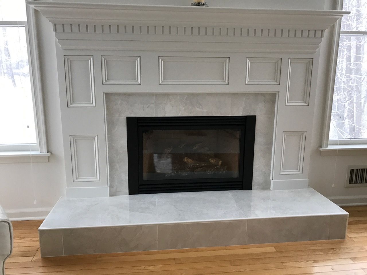 White fireplace mantel with black firebox and light stone hearth in a bright living room
