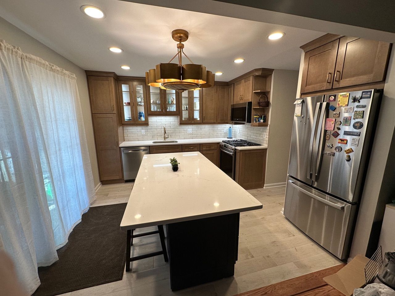 Modern kitchen with island, white counters, wood cabinets, and stainless steel refrigerator