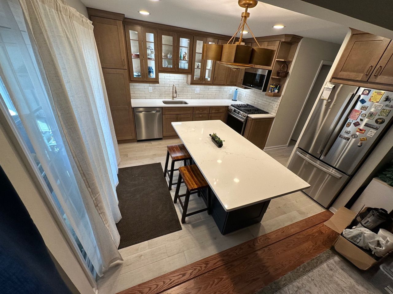 Bright kitchen with island, white cabinets, stainless fridge, and sheer curtains by a sliding glass door