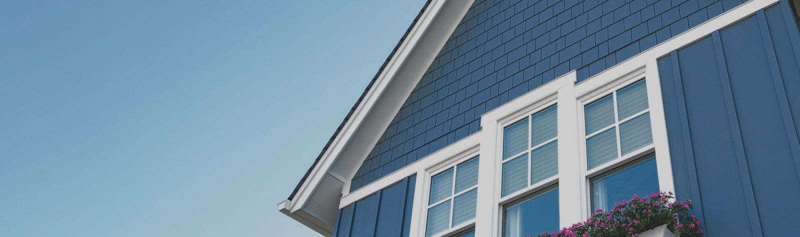 Blue house exterior with white-trimmed windows and gabled roof against a clear sky