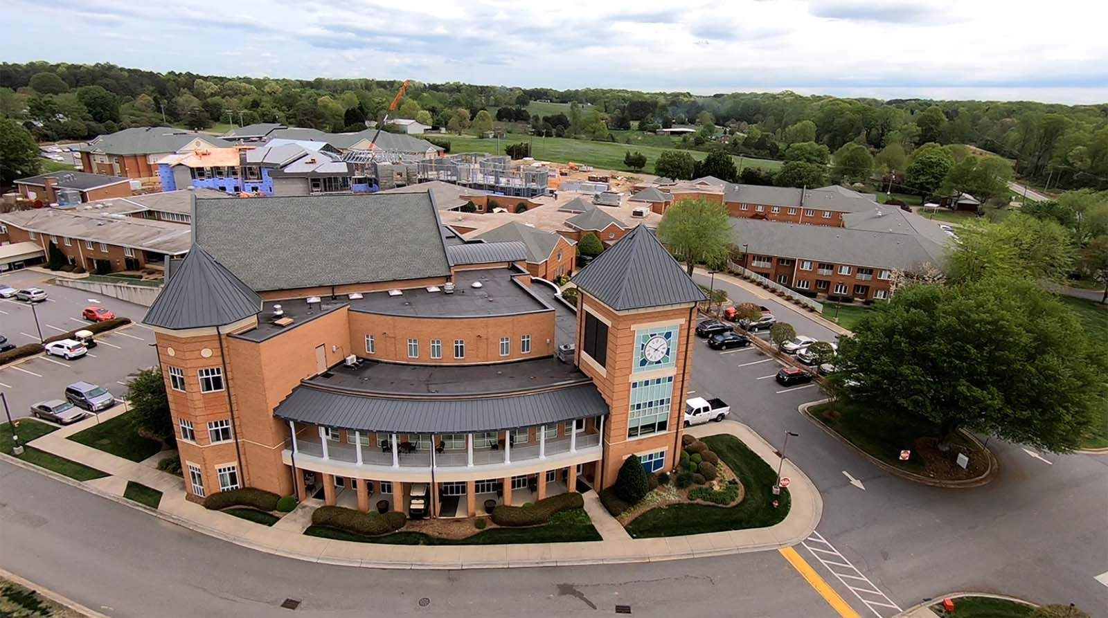 Aerial view of a large brick building with a turret, curved entrance, and parking lot surrounded by trees.
