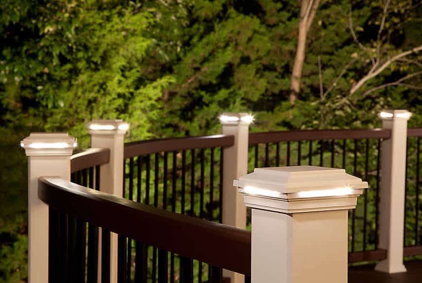 Wooden deck railing with white posts overlooking green trees