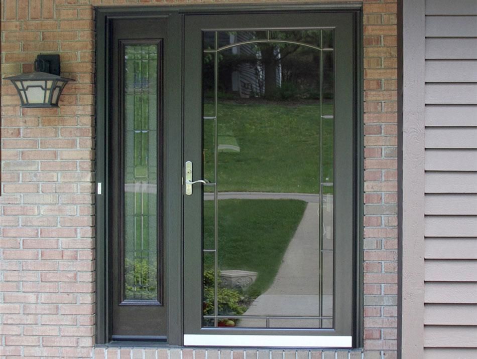 Front entrance with a dark green glass door, sidelights, brick wall, and porch light.
