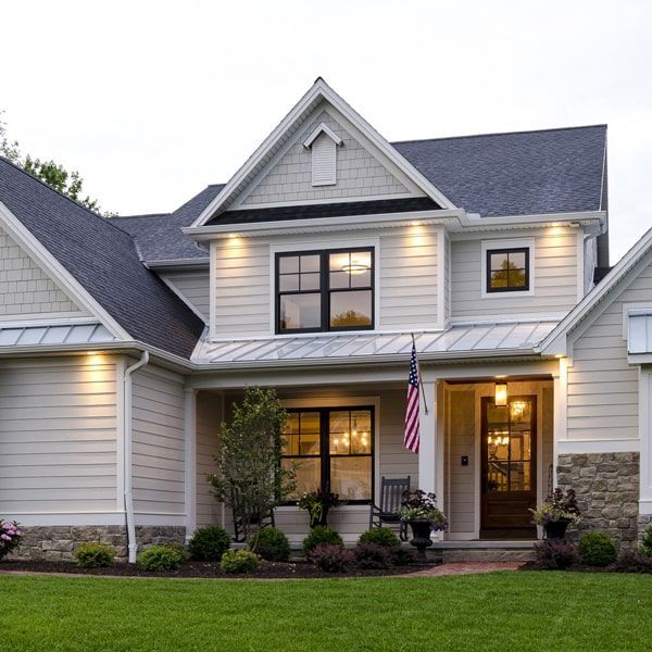 Suburban two-story house with lit windows, front porch, American flag, and manicured lawn at dusk