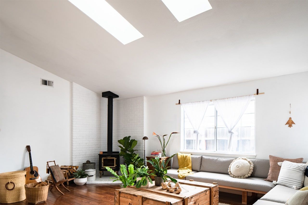 Bright living room with skylights, wood stove, large window, plants, and a gray sectional sofa