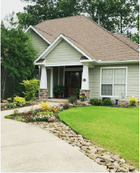 Suburban house with tan roof, white siding, curved driveway, and landscaped front yard.