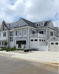 Gray coastal-style house with white trim, garage, and driveway under a cloudy sky