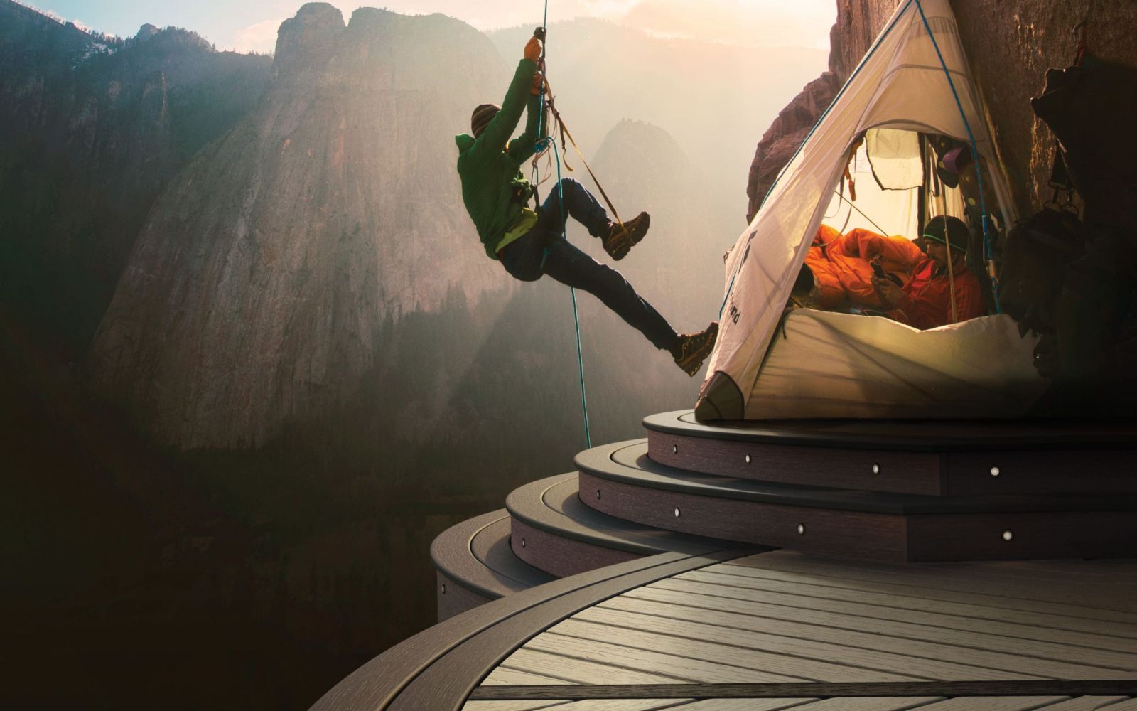 Climber swings on a rope beside a tent on a cliffside overlook at sunset.