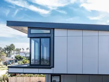 Modern building corner with large glass windows and a blue roof against a cloudy sky