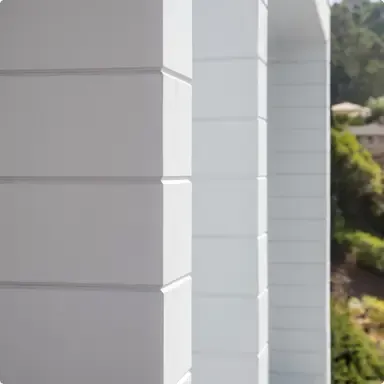 White building corner with horizontal siding and a green hillside in the background