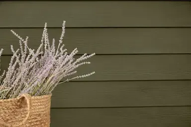 Woven basket with pale lavender stems against a dark green wooden wall