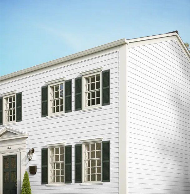 White two-story house exterior with dark green shutters and a front door under a blue sky