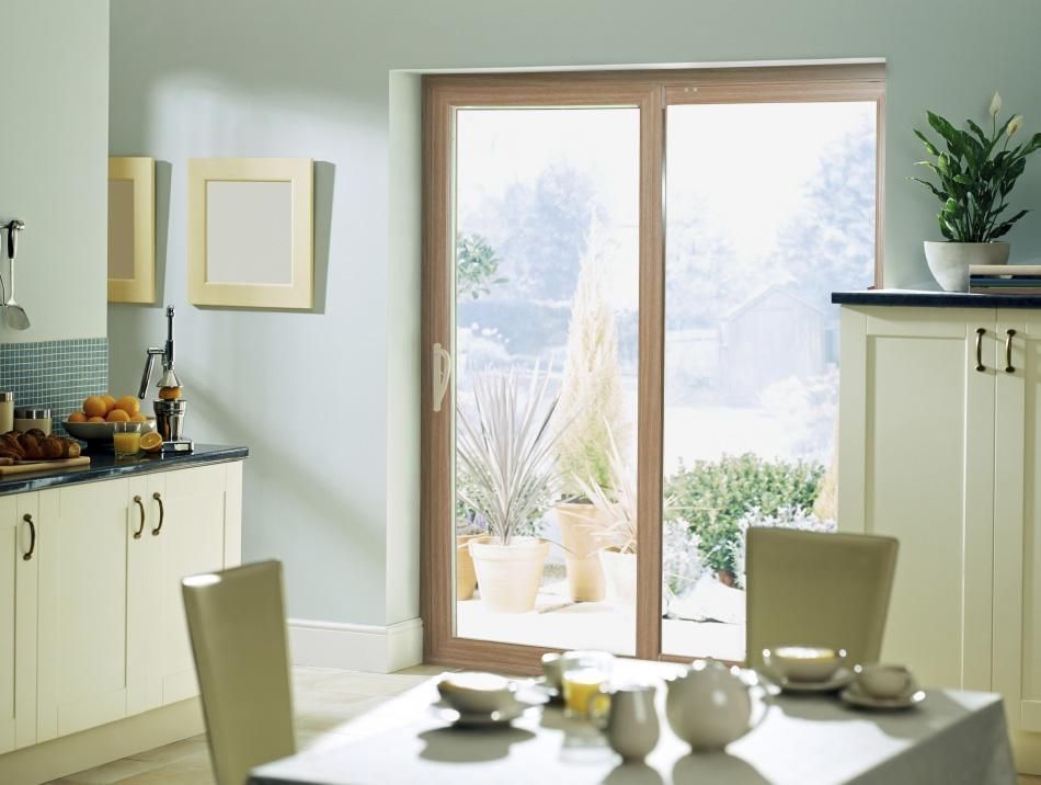 Bright kitchen with cream cabinets, dining table, and sunlit glass doors opening to a patio with plants