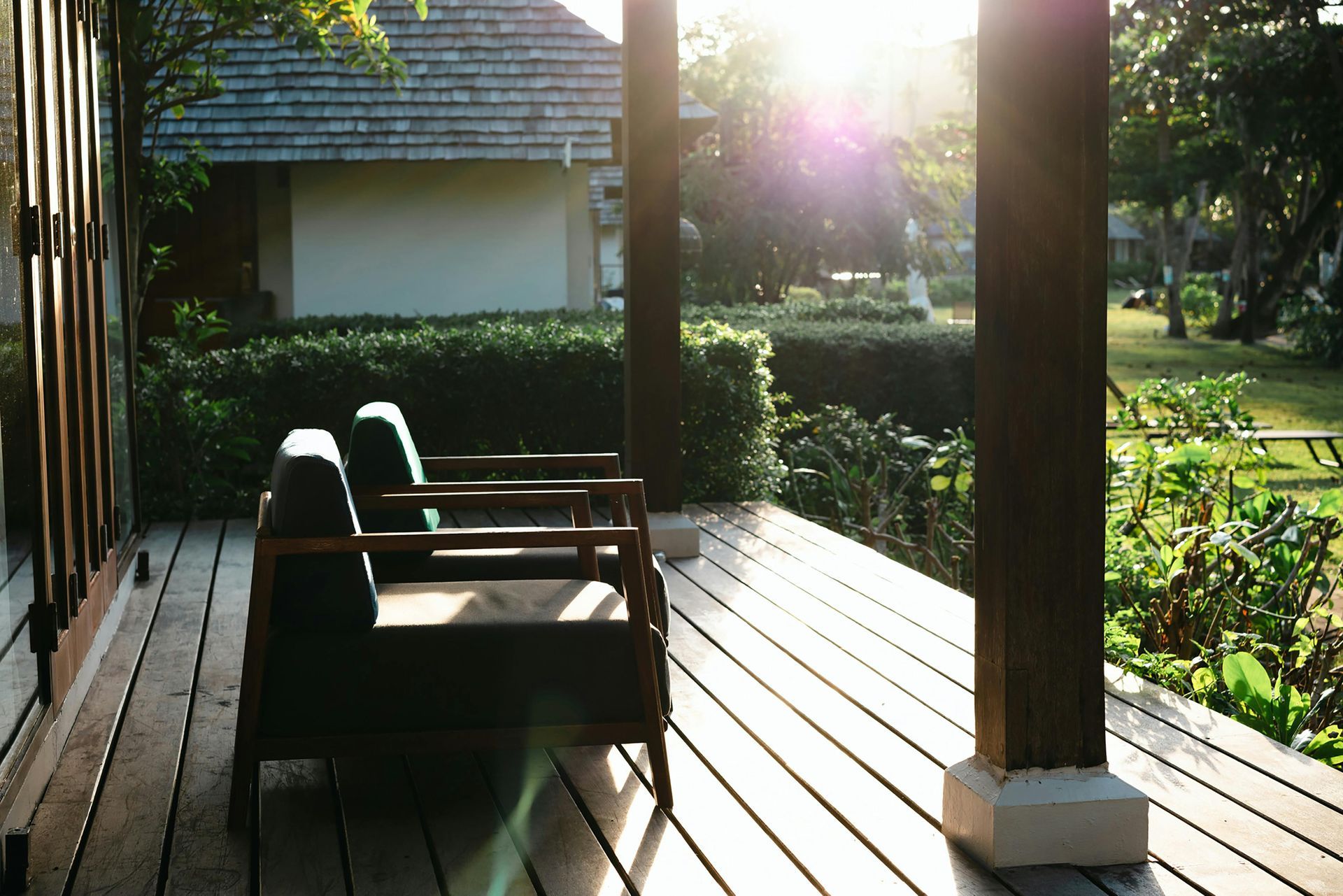 Wooden porch with chairs facing a sunlit garden and a house in the background