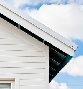 White house gable with horizontal siding and a dark roof edge against a blue sky with clouds