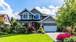 Suburban two-story house with a manicured green lawn, white garage, and pink flowers in front