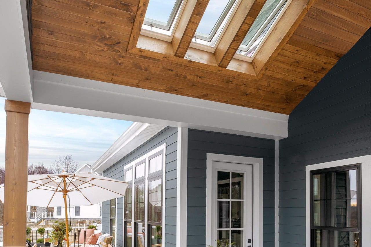 Covered porch with wood ceiling, skylights, and dark gray house exterior overlooking a snowy neighborhood