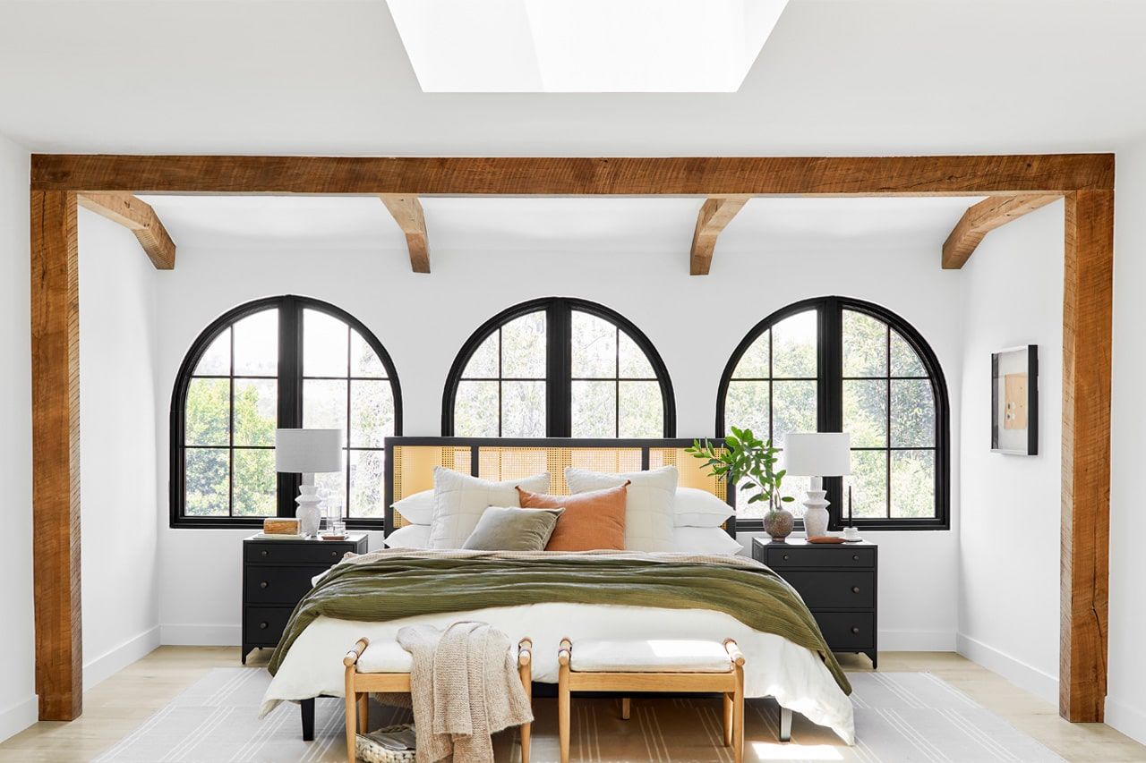 Bright bedroom with arched windows, exposed beams, and a bed with green bedding and wooden bench.