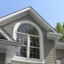 White arched window with divided panes on a gray house beneath a blue sky