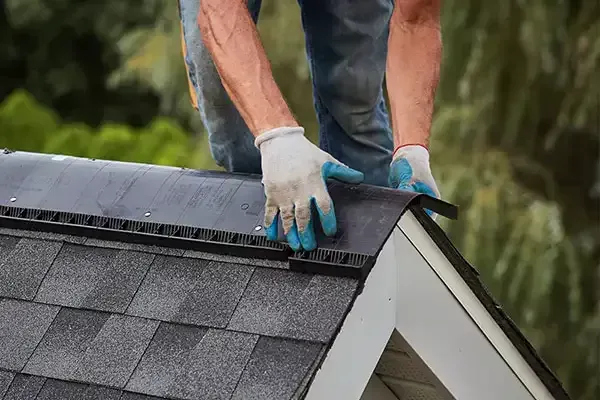 Worker installing black shingles on a roof ridge wearing blue gloves