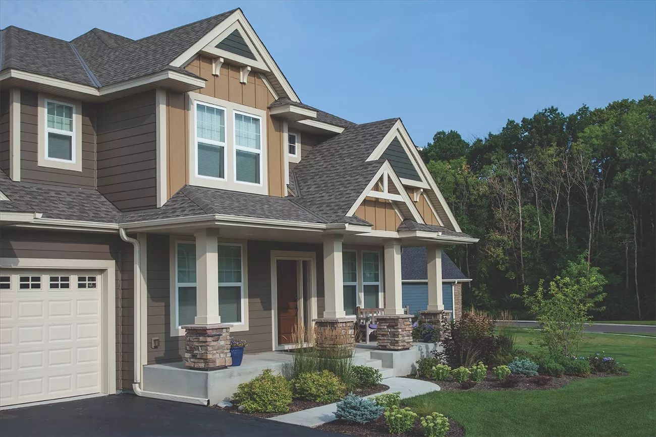 Suburban house with brick and siding exterior, front porch, garage, and landscaped yard under a blue sky