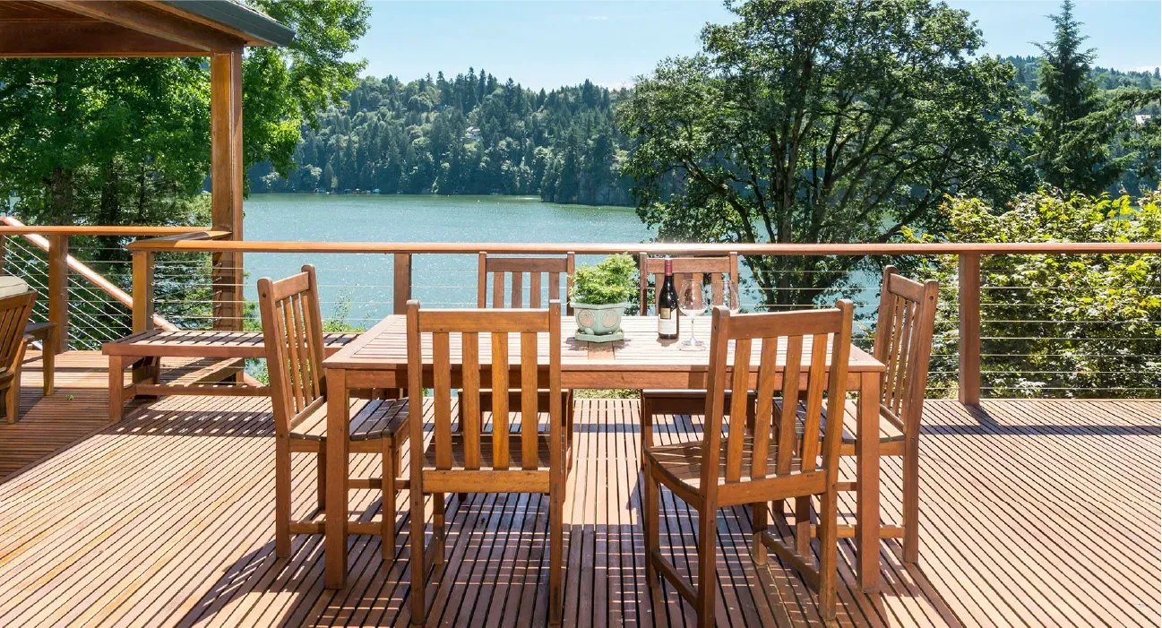 Wooden deck dining set overlooking a sunny lake and wooded shoreline