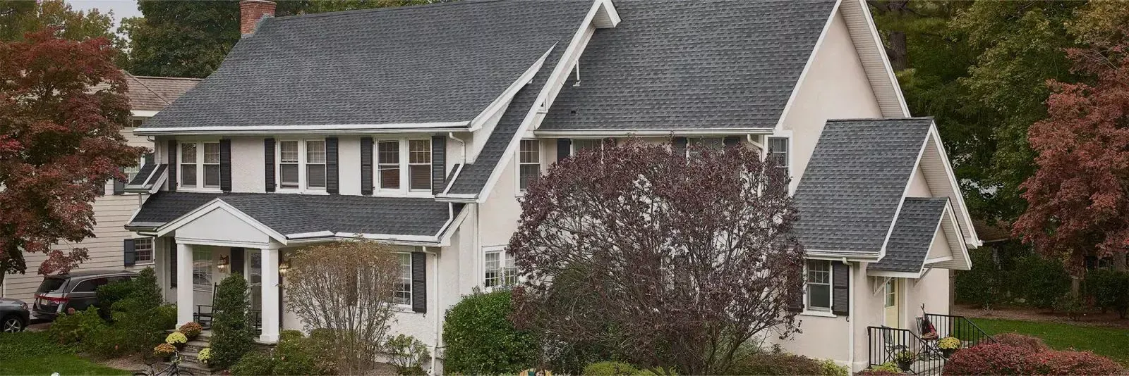 Suburban house with gray roof, white siding, and front porch surrounded by trees and shrubs