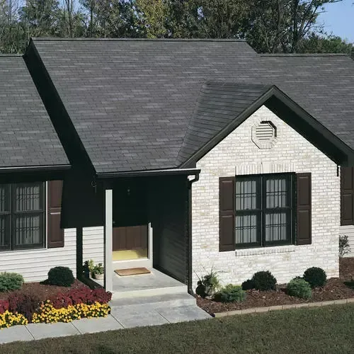 Suburban house exterior with dark roof, white brick facade, covered porch, and landscaped front garden