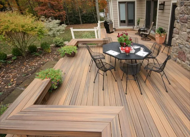 Wooden backyard deck with black patio table, chairs, potted plants, and landscaped garden.
