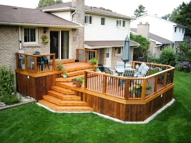 Backyard deck with wooden railings, stairs, and patio furniture beside a house and green lawn